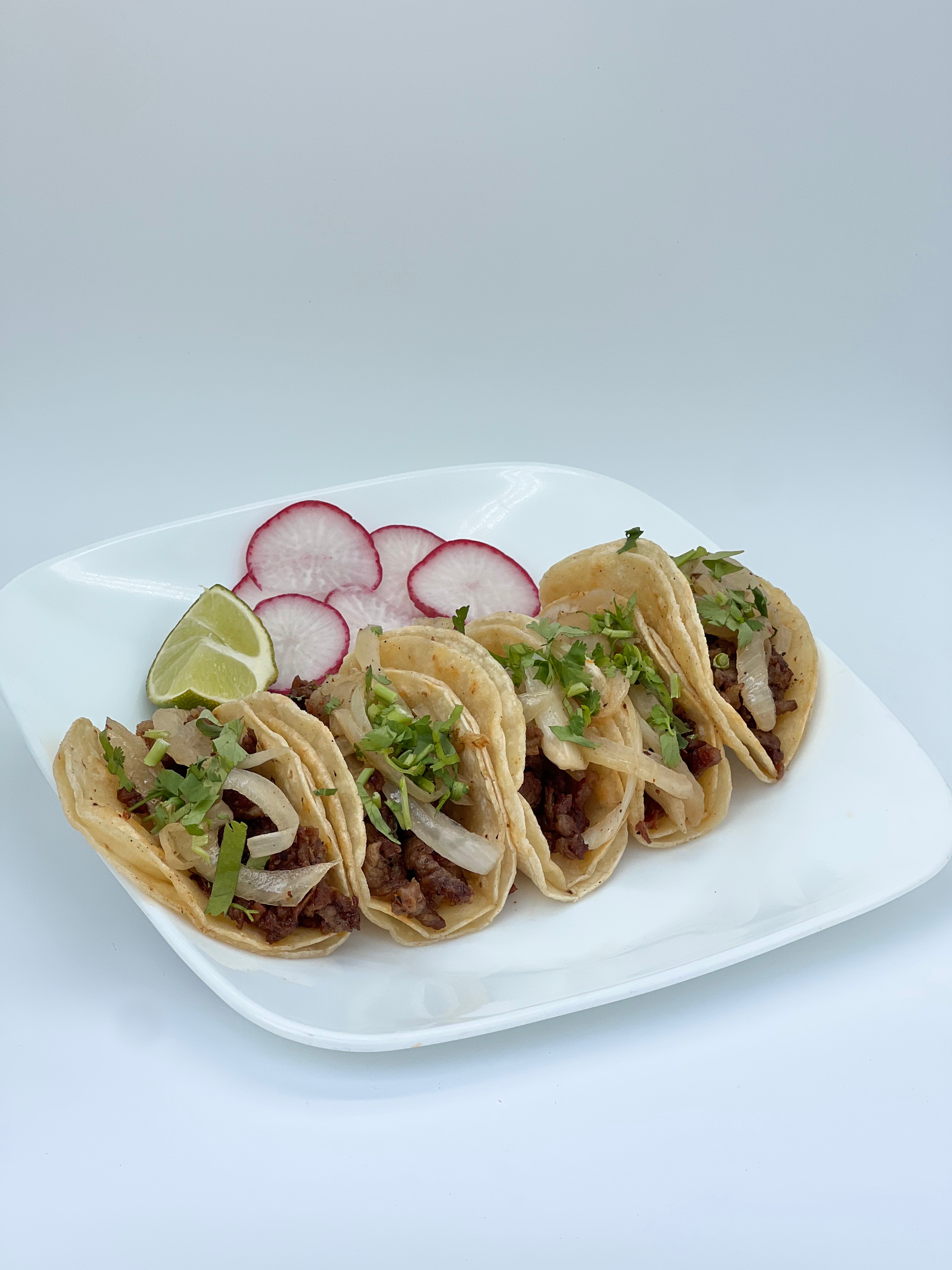 La Herradura street tacos topped with onion and cilantro, served with lime and radishes